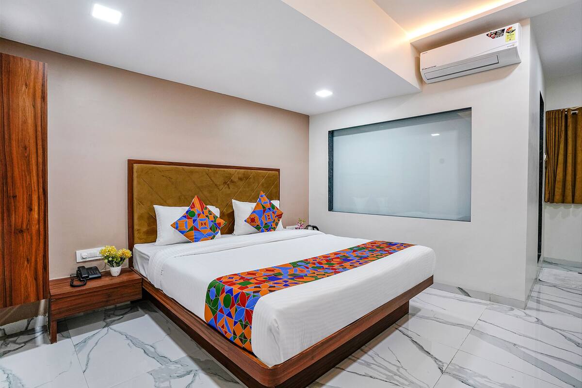 A hotel room with a large bed, a wooden headboard, a nightstand with a phone and a vase of flowers, and a large window.
