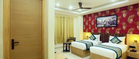 A hotel room with two beds, a ceiling fan, a desk, and a chair.