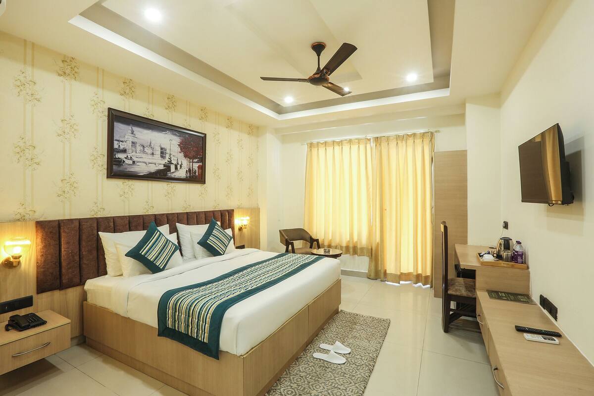 A hotel room with a bed, bedside table, lamp, chair, desk, television, and a ceiling fan.
