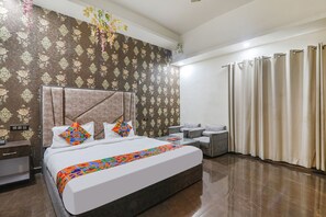 Una habitación de hotel con una cama grande, una mesa de centro de vidrio, un sofá y cortinas.