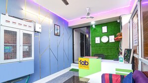 A hotel reception area with a green wall, a reception desk, and a seating area with a purple couch. - Fabhotel The Sunshine Residency (Barasat)