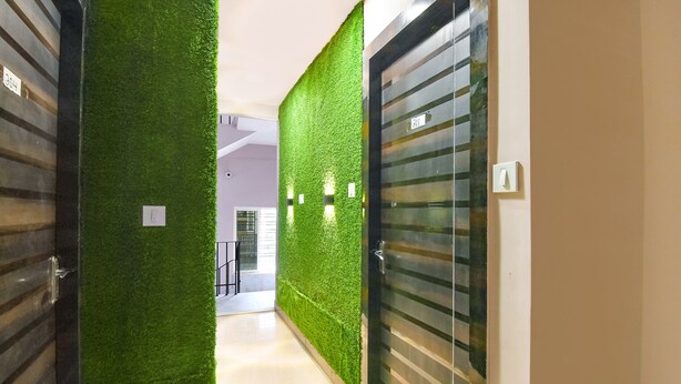 A hallway with green artificial grass walls, a glass door with a number, and a light switch. - Fabhotel The Sunshine Residency (Barasat)