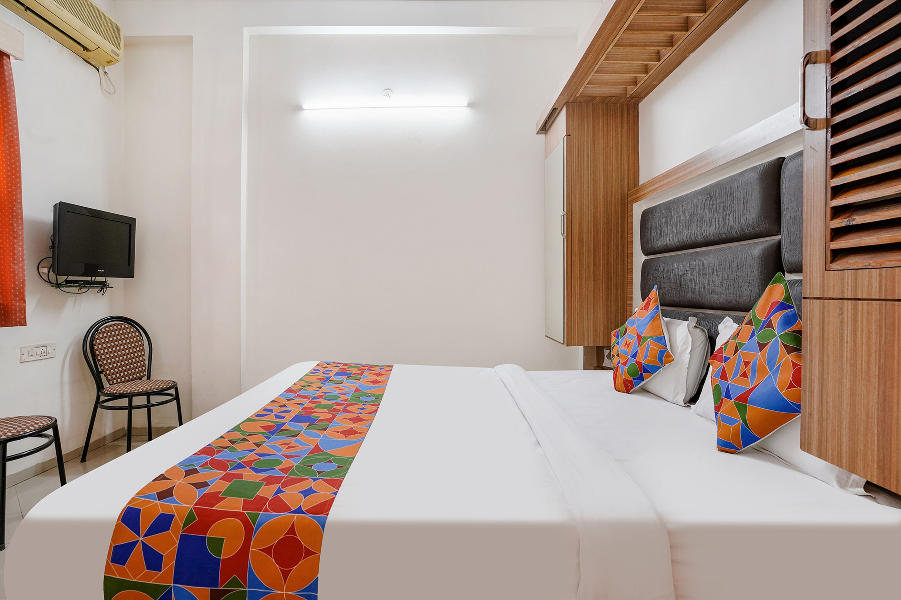 Hotellihuone, jossa on sänky, tuoli, televisio ja puinen pääty.