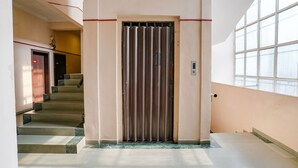 A staircase leading to an elevator in a building with a light-colored interior and large windows. - Fabexpress Shanti Inn (Nashik)