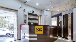 A reception desk with a 'fab hotels' sign, a ceiling fan, and a view of the street outside. - Fabexpress Shanti Inn (Nashik)