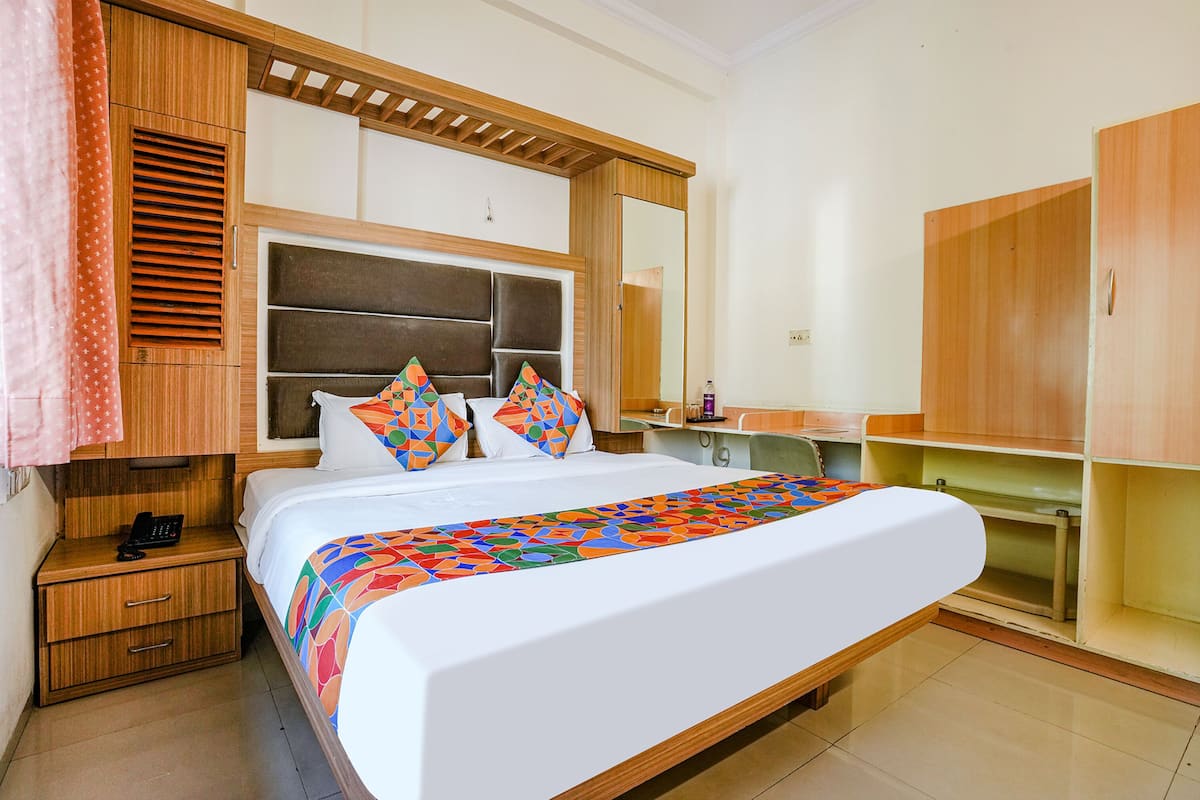 A hotel room with a large bed, wooden headboard, a bedside table with a phone, and a wardrobe.