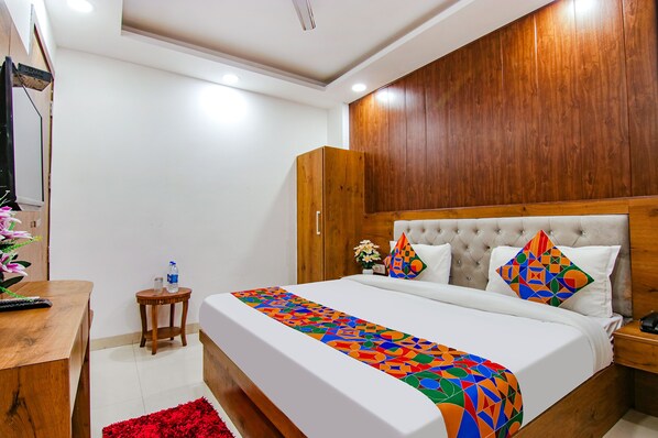 A bedroom with a large bed, wooden headboard, and a colorful geometric bedspread. - Fabhotel The Glory I (New Delhi)