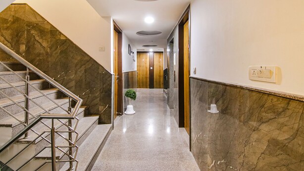 A modern hotel hallway with marble flooring, a glass staircase, and a wooden door at the end. - Fabhotel The Glory I (New Delhi)