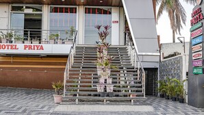 Entrada d'hotel amb una escala que condueix a l'entrada, plantes en testos i un rètol que enumera serveis com aire condicionat, saló i opcions gastronòmiques.