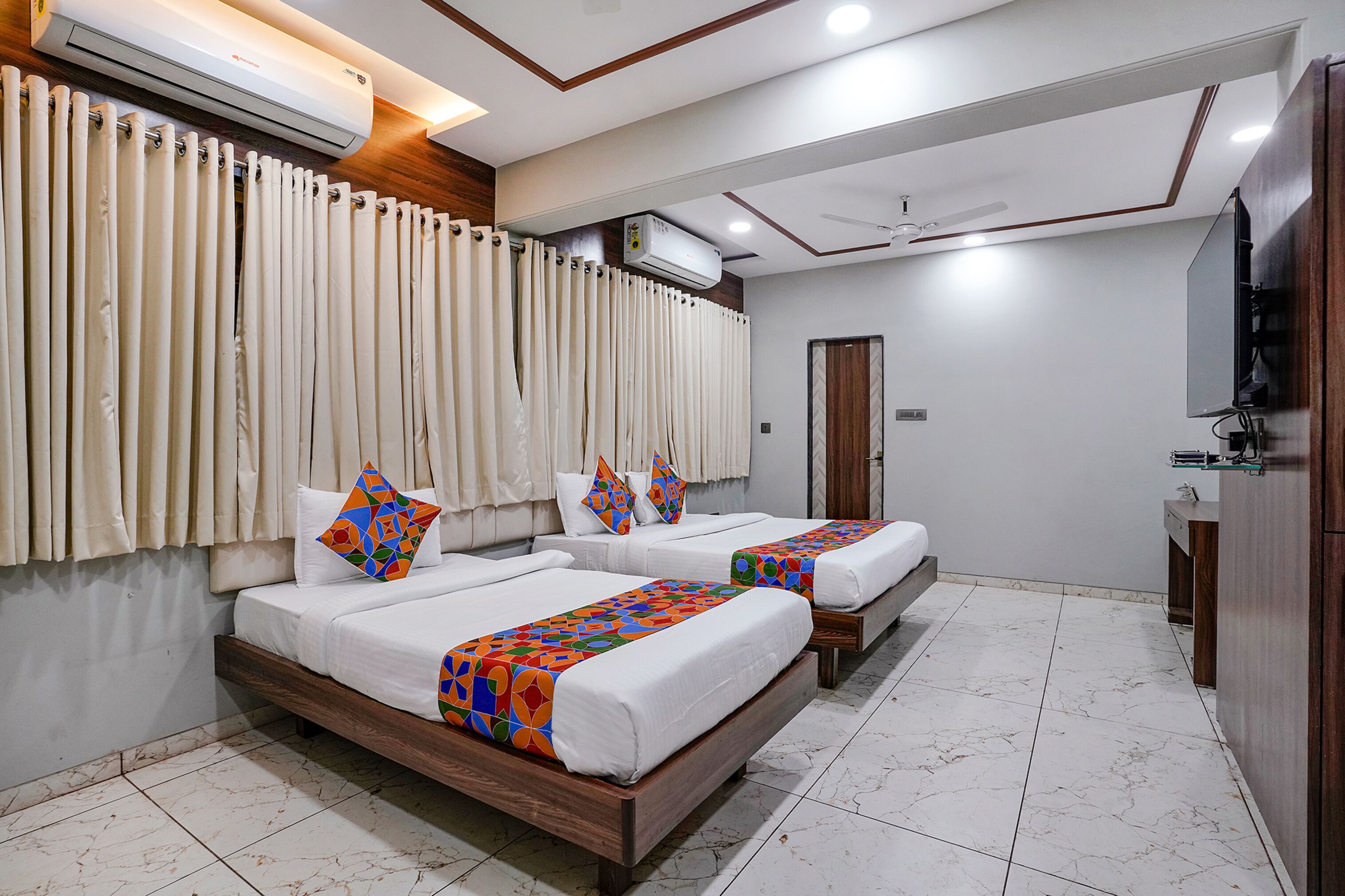 A hotel room with two beds, a wooden headboard, a ceiling fan, an air conditioning unit, a TV, and a wooden wardrobe.