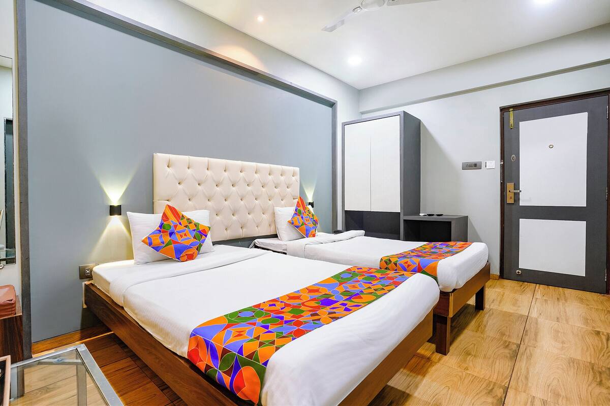 A hotel room with two beds, a large window, a wardrobe, and a bedside table.