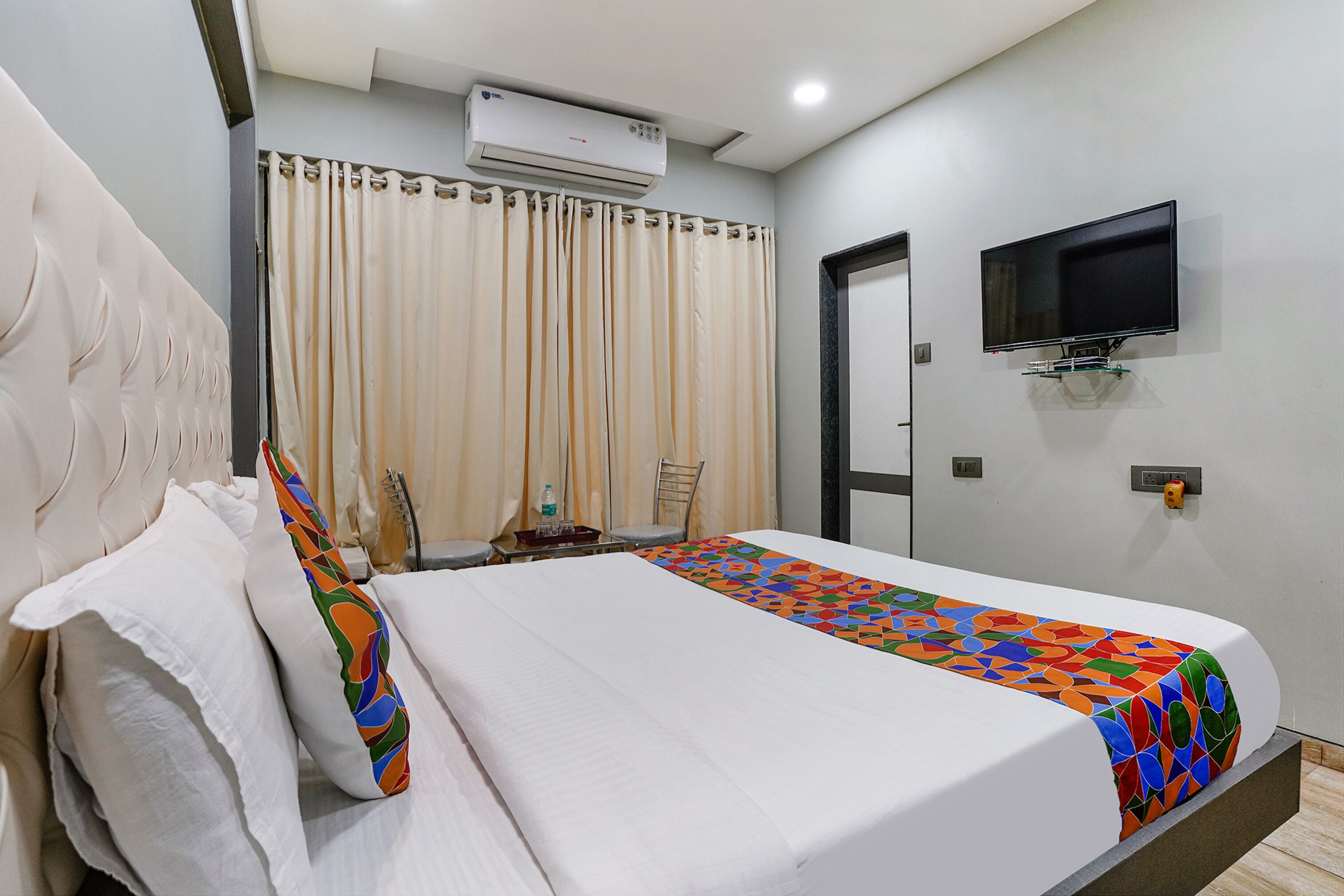 A hotel room with a bed, a television mounted on the wall, an air conditioning unit, and a door.