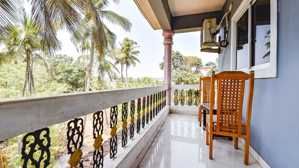 A balcony with a railing, a wooden chair, and a window with an air conditioning unit. - Via Tasty Buds - 300m From Calangute Beach (Baga)
