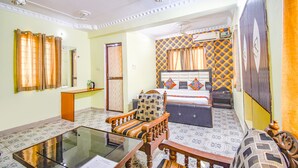 A hotel room with a bed, a sofa, a wooden chair, a glass table, a mirror, and a ceiling fan. - Fabhotel Golden Horizon (Ranchi)