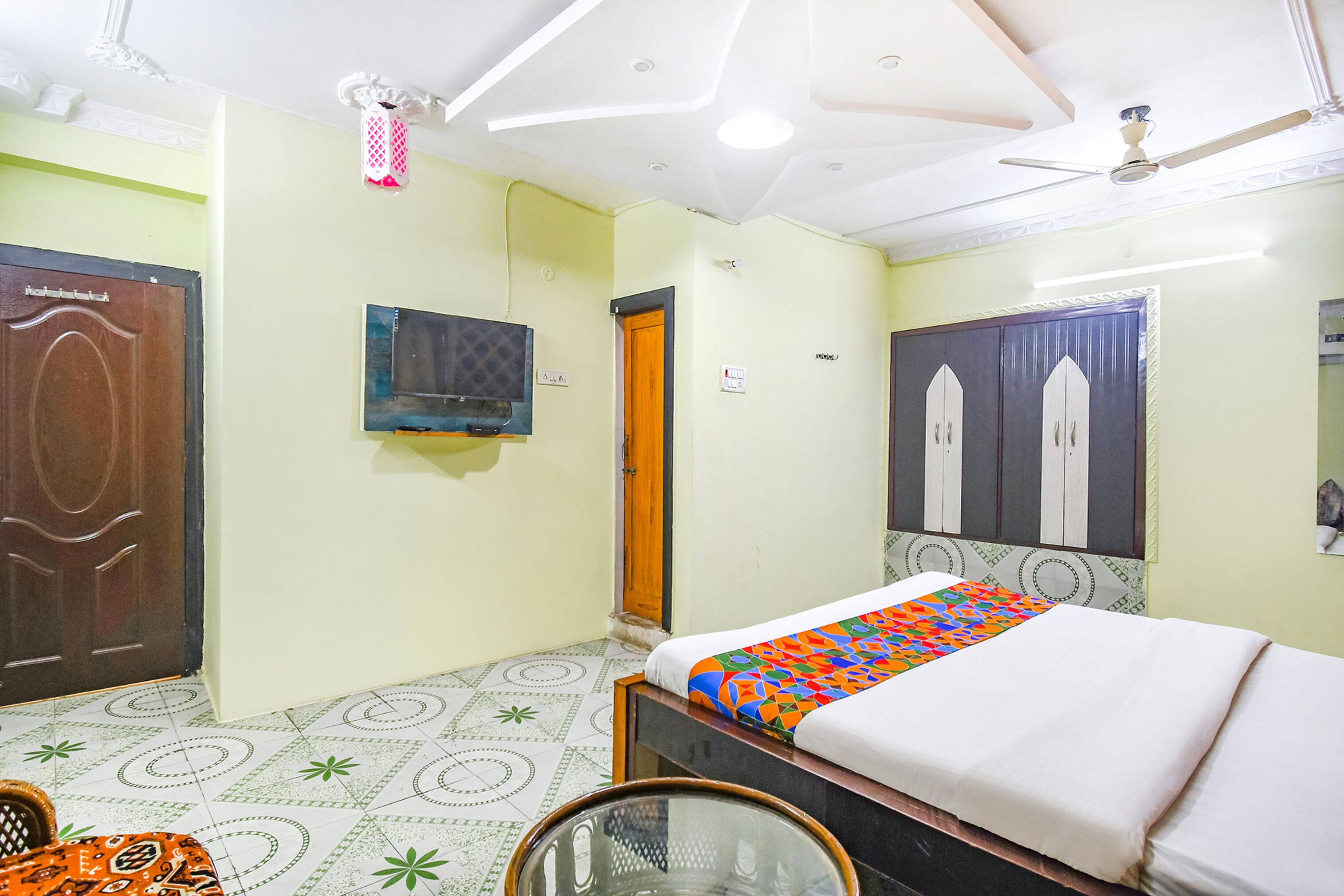 Ein Hotelzimmer mit Bett, Fernseher, Deckenventilator und einer Tür.