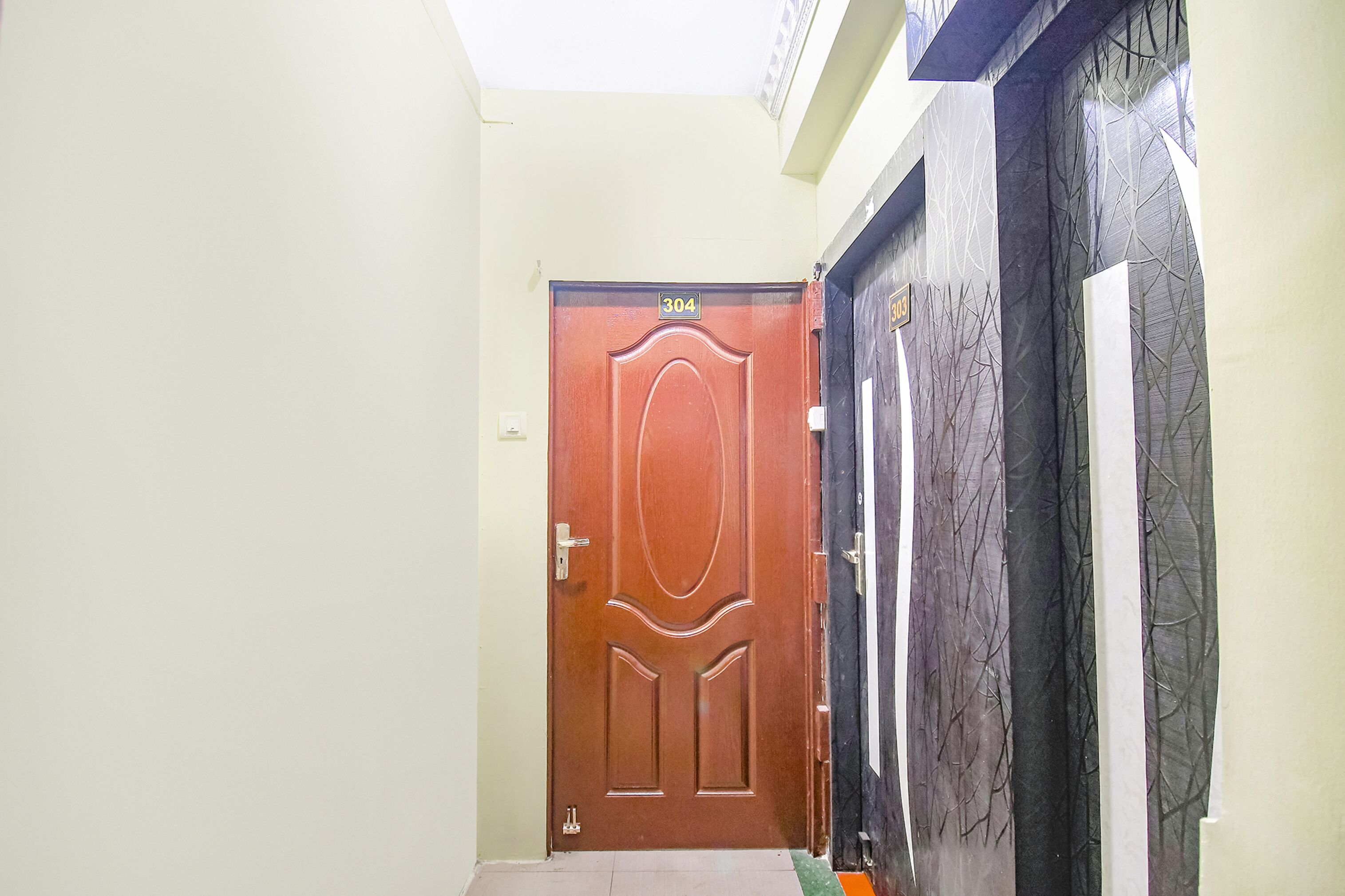 A hallway with a wooden door labeled 304, a black door with a tree branch design, and a white door with a similar design.