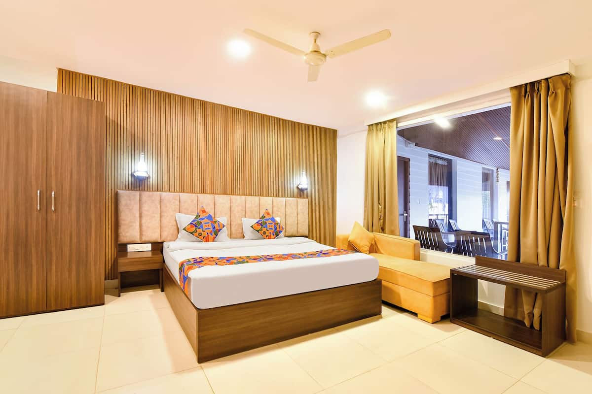A modern hotel room with a large bed, wooden wardrobe, and a view of the outdoor seating area.