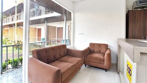 A modern hotel room with a large window, a sofa, a chair, and a wooden counter. - FabHotel Morjim Bliss - Nr. Morjim & Ashwem Beach (Morjim)