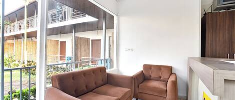 A modern hotel room with a large window, a sofa, a chair, and a wooden counter.