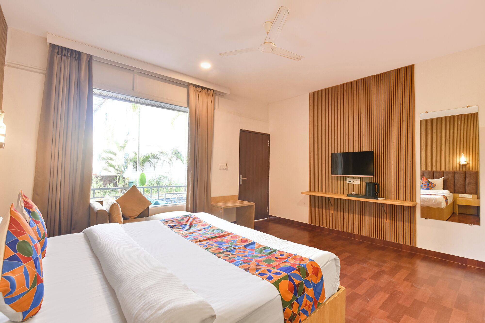 A hotel room with a large bed, a TV, a wooden panel wall, and a balcony with curtains.