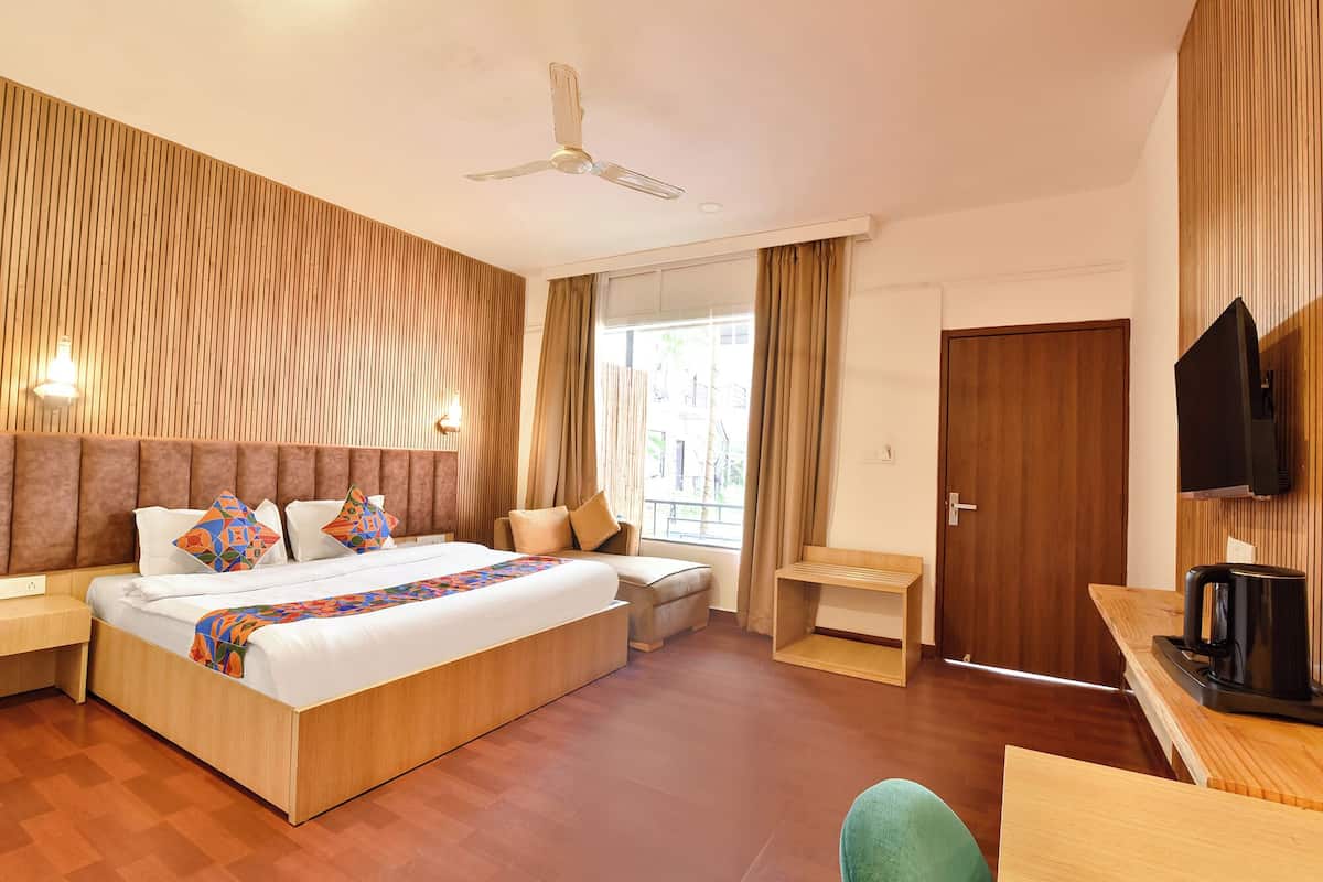 A modern hotel room with a large bed, a desk, a chair, a TV, and a ceiling fan.