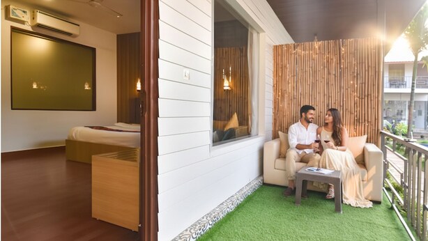 A modern hotel room with a bed, a seating area with a sofa and a small table, and a balcony with a view. - FabHotel Morjim Bliss - Nr. Morjim & Ashwem Beach (Morjim)