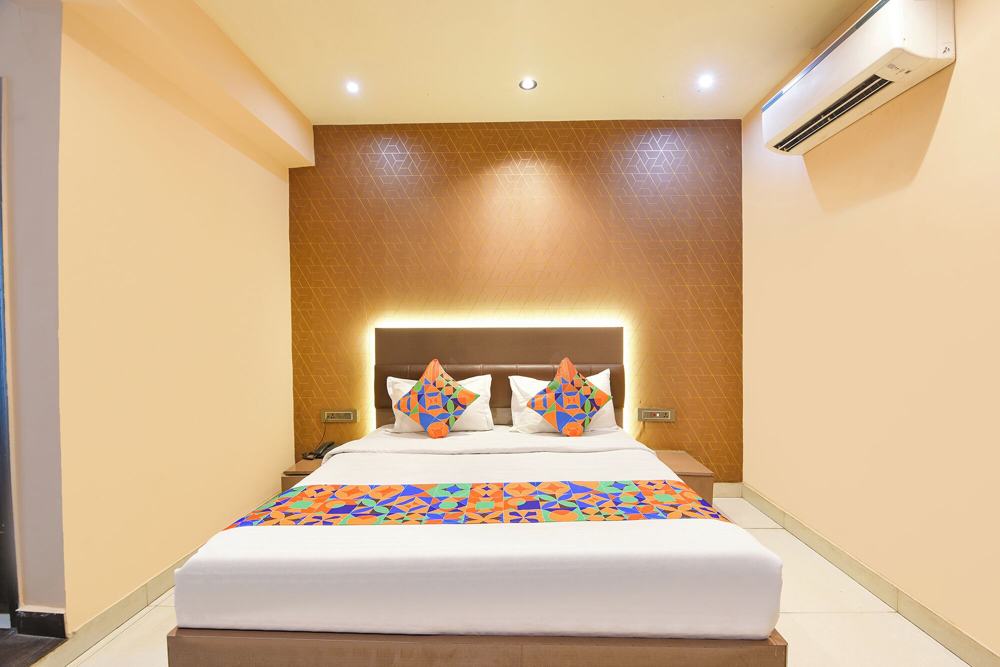 Une chambre d’hôtel comprenant un lit, une tête de lit, un appareil de climatisation et un mur orné d’un motif géométrique.