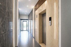 A modern hallway with a marble floor, a wooden panel wall, and an elevator with a control panel. - Fabhotel 19 West (New Delhi)