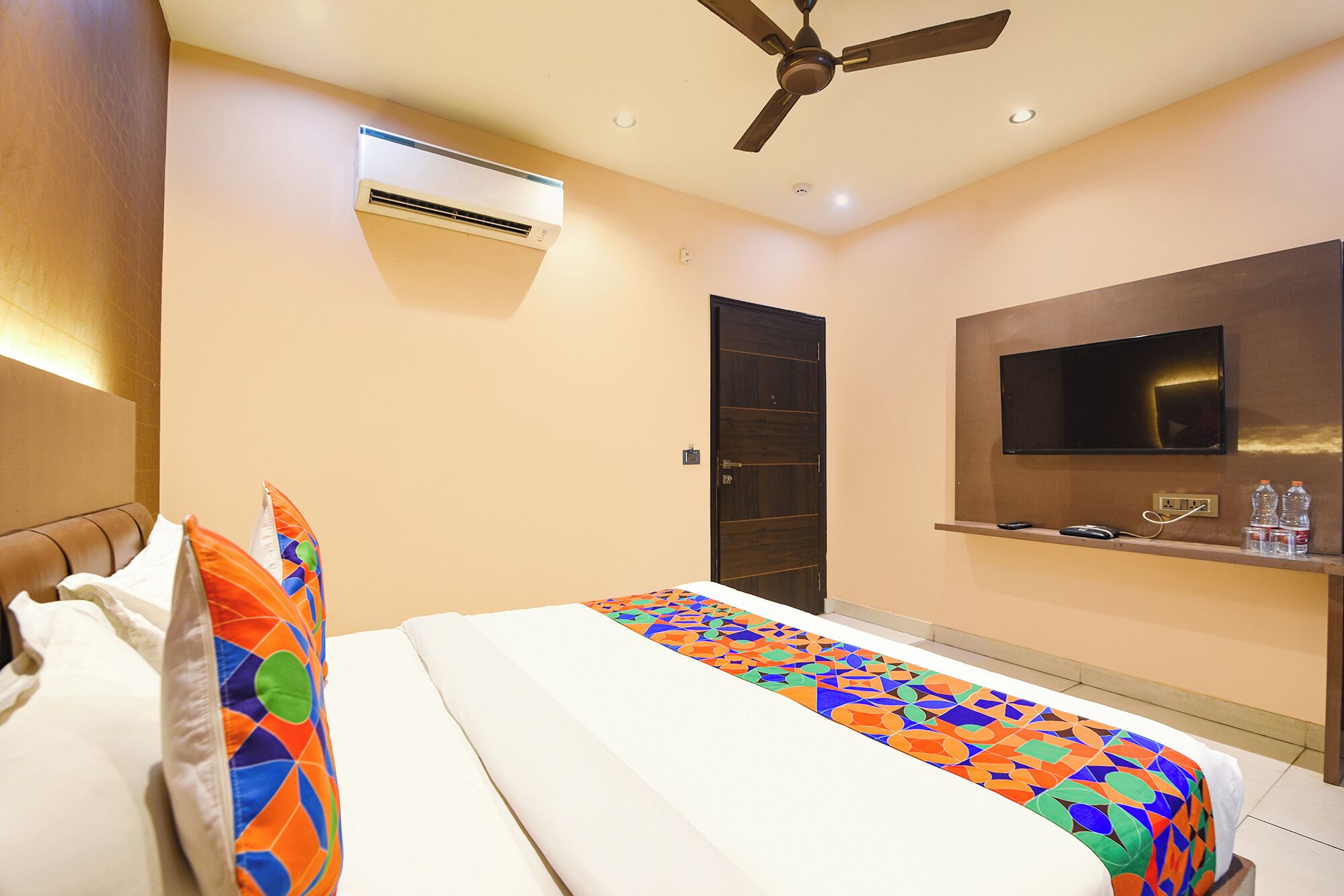 A hotel room with a bed, a ceiling fan, an air conditioning unit, a television, and a minibar.