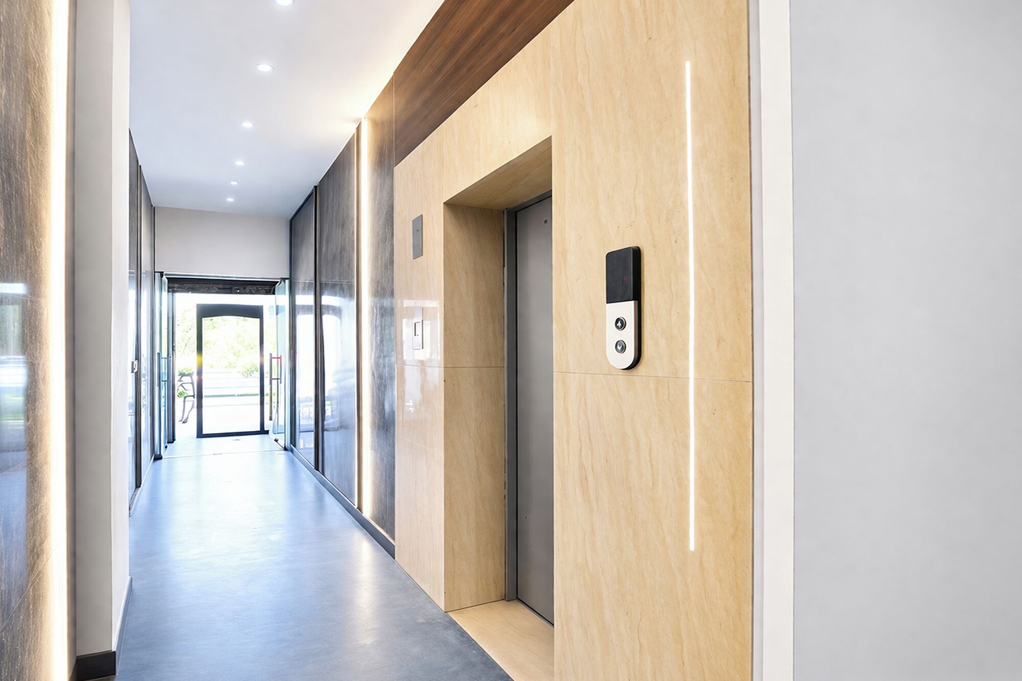 A modern hallway with a wooden panel wall, a wall-mounted elevator, and a glass door leading to an outdoor area.