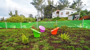 A garden with variously colored pots containing plants, a green fence, and a white building in the background. - FabHotel All Season's Stays (Ootacamund)