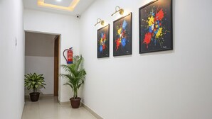 A hallway with three abstract paintings on the wall, a fire extinguisher, and two potted plants. - Fabhotel White House Inn (Pune)