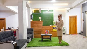 A hotel reception area with a reception desk, a sofa, a small table with a vase, and a sign that reads "FAM HOTEL". - Fabhotel White House Inn (Pune)