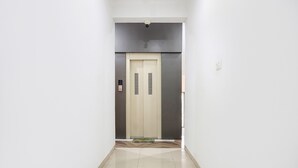 A hallway leading to an elevator with a plain door and a security camera above. - Fabhotel White House Inn (Pune)