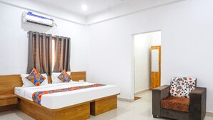 A hotel room with a wooden bed, a sofa, an air conditioning unit, and a door leading to another room. - Fabhotel White House Inn (Pune)