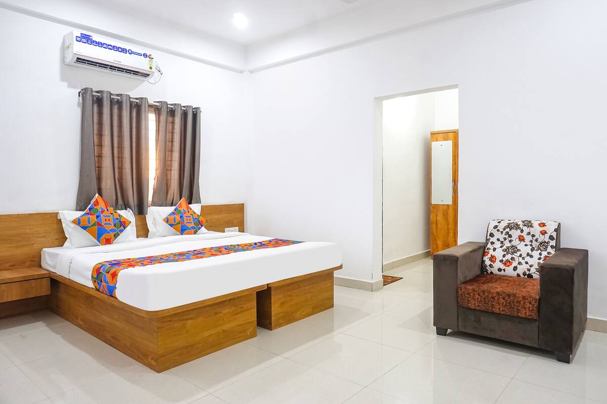 A hotel room with a wooden bed, a sofa, an air conditioning unit, and a door leading to another room.