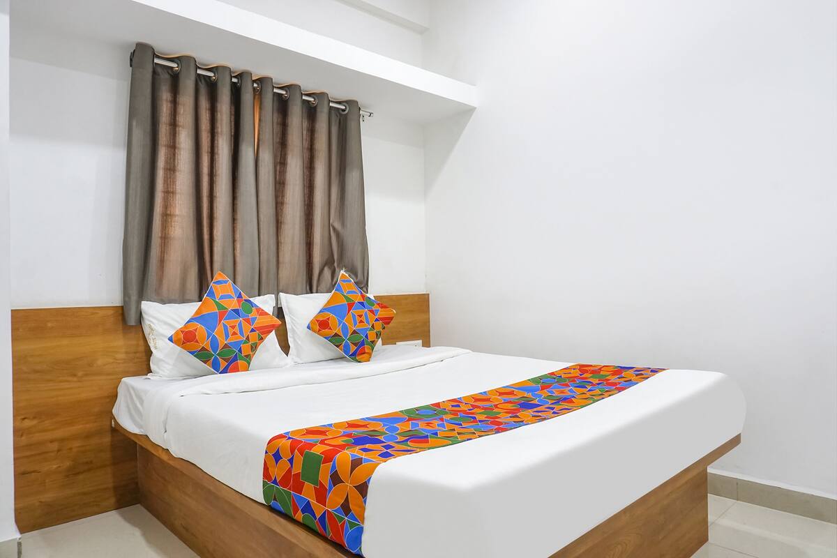 A neatly made bed with a colorful geometric-patterned throw, a wooden headboard, and a curtain.
