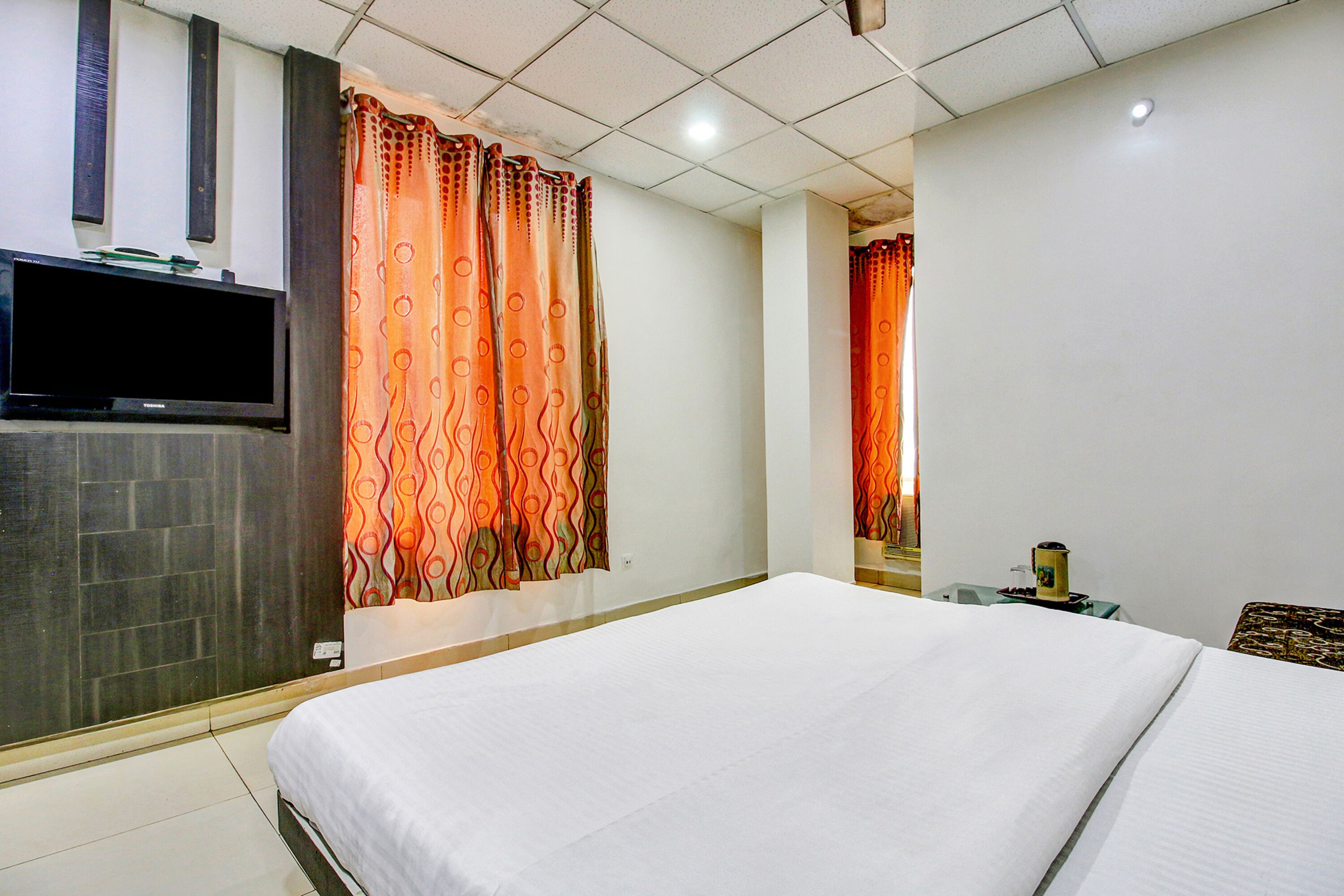 A hotel room with a large bed, a flat-screen TV mounted on the wall, and orange patterned curtains.