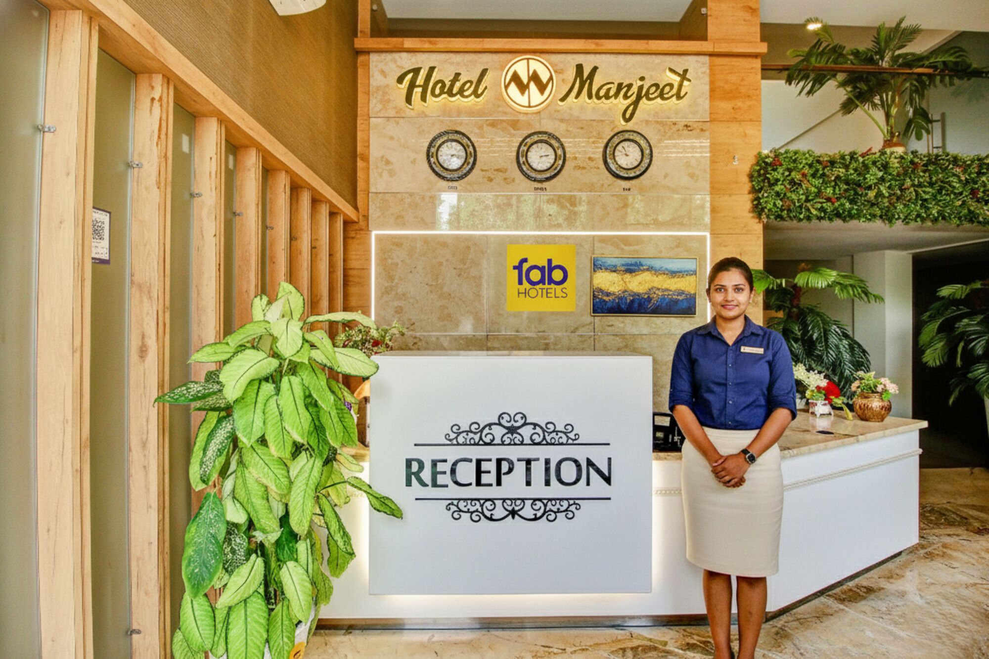 A reception desk at Hotel Manjeet with a 'fab hotels' sign, a clock, and a reception sign.