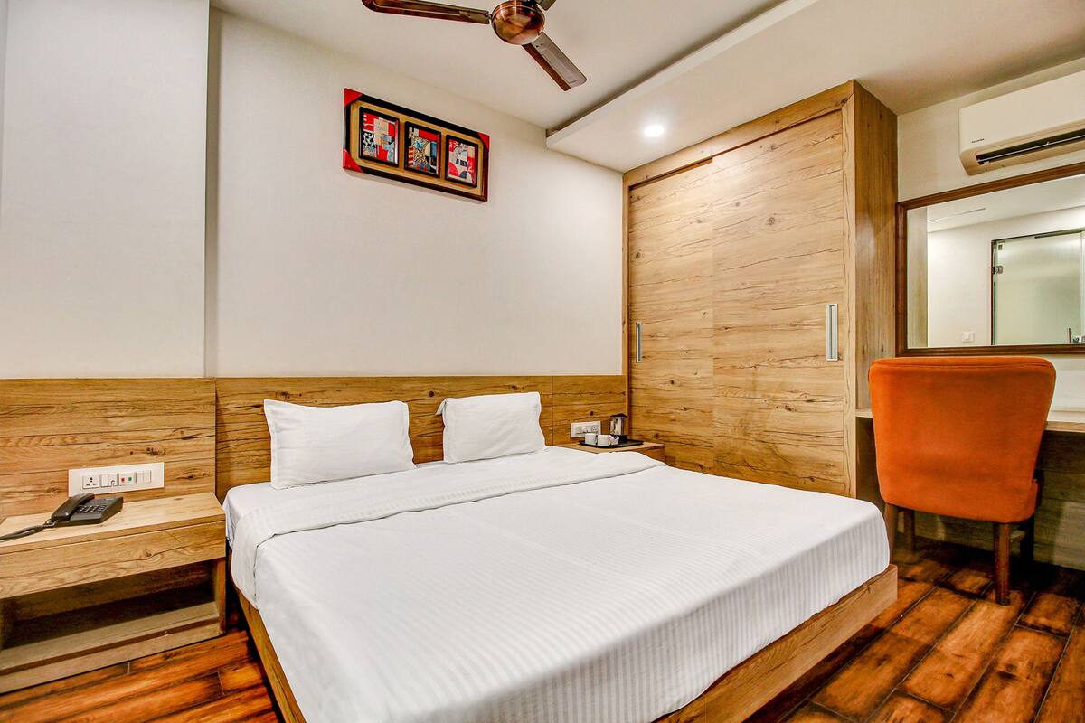 A hotel room with a wooden headboard, a bed with white bedding, a nightstand with a phone, a wooden chair, and a ceiling fan.