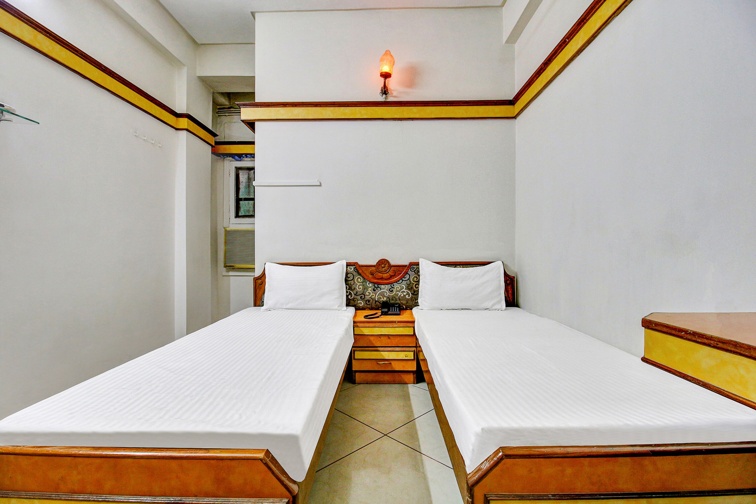 A room with two single beds, a small table, and a wall-mounted light fixture.
