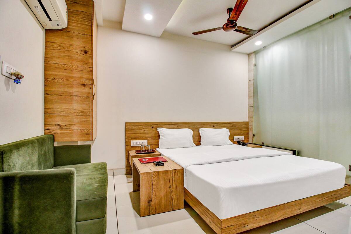 A modern hotel room with a wooden headboard, a green armchair, a wooden nightstand, and a ceiling fan.
