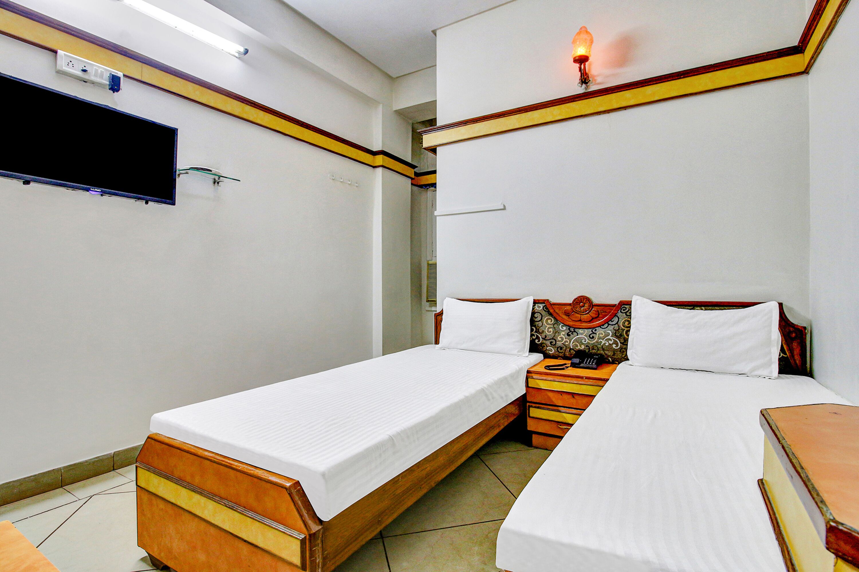 Une chambre d’hôtel avec deux lits simples, un téléviseur à écran plat fixé au mur et une table de chevet avec une lampe.