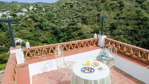 Eine Terrasse mit Tisch für zwei Personen, umgeben von einer Brüstung, mit Blick auf eine Hügellandschaft und verstreute Gebäude.