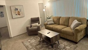 En stue med en beige sofa, en brun lænestol, et sofabord og en tæppe med et mønster.