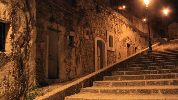 En stentrappe fører op til en bygning med buegange og en stenvæg.