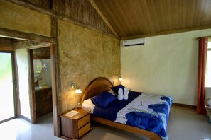 Une chambre avec une tête de lit en bois, un lit recouvert d’une couette bleue, deux lampes de chevet, une table de chevet et un appareil de climatisation fixé au mur.