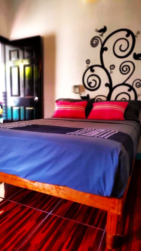 A bed with a blue bedspread and red pillows, a wooden headboard, and a wall with a black decorative pattern.