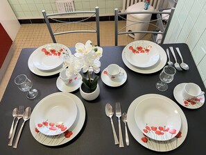 A beautifully set dining table features white plates with floral designs, silver cutlery, and a vase with white orchids.