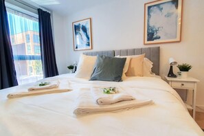 A hotel room with a large bed, two pillows, a nightstand with a lamp, and two framed artworks on the wall. - Beautiful 1-bed Apartment in Gloucester (Gloucester)